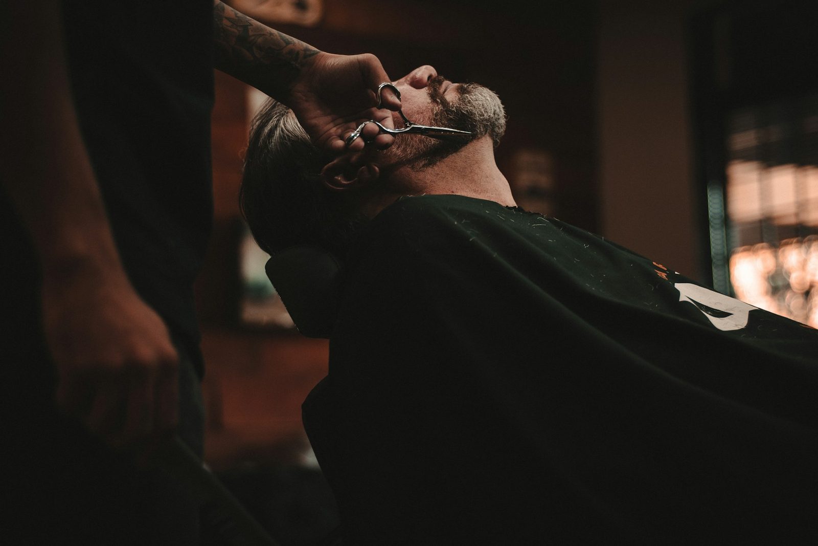 Barber giving a hot towel shave in a dark shop